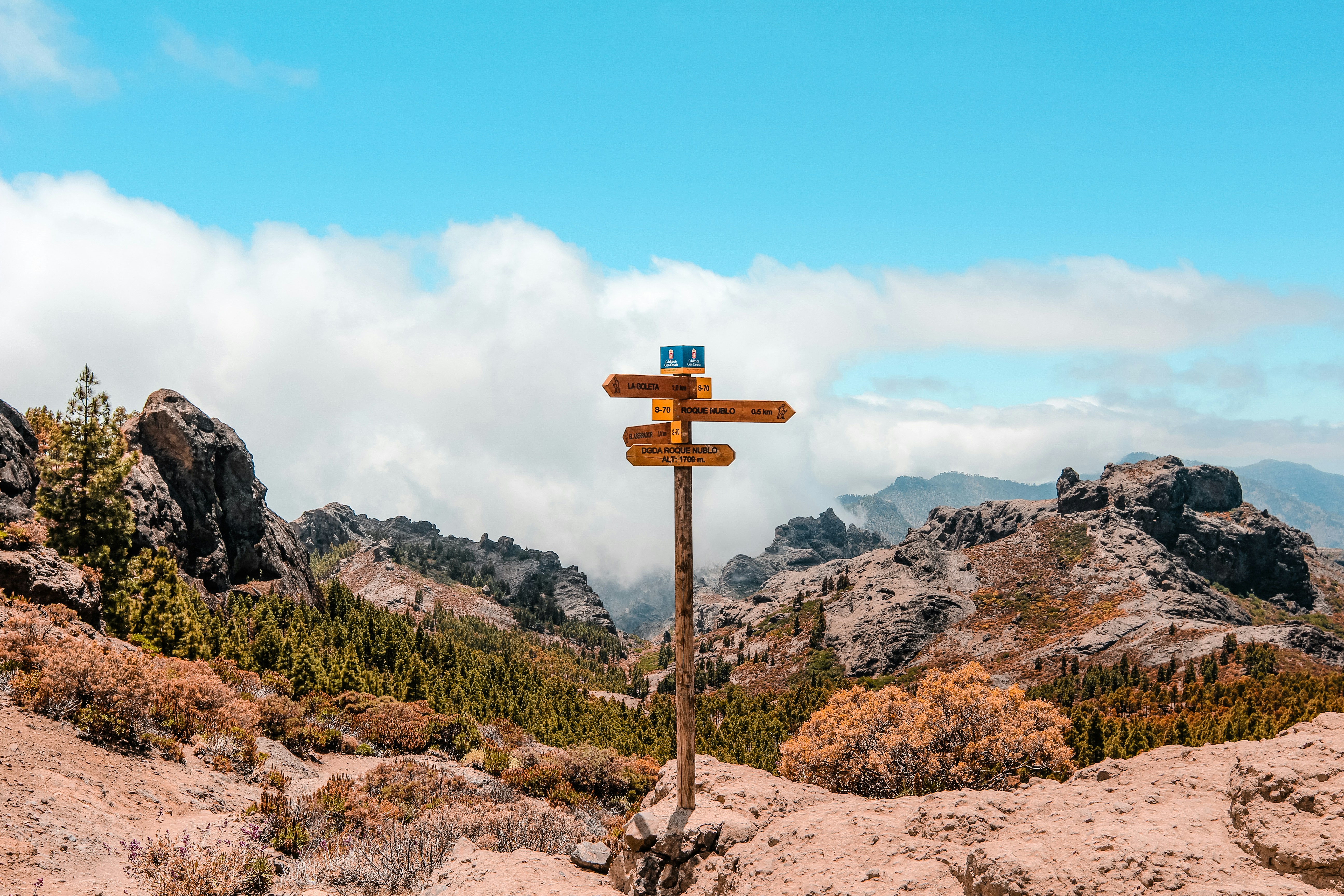 brown wooden arrow sign on rocky hill under blue and white sky during daytime