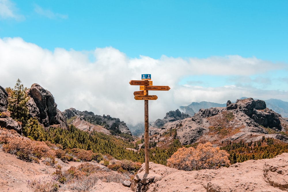 brown wooden arrow sign on rocky hill under blue and white sky during daytime