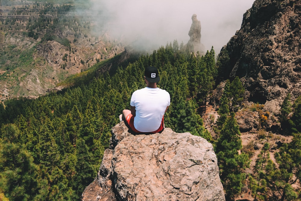 白いTシャツを着た崖の上に座る男