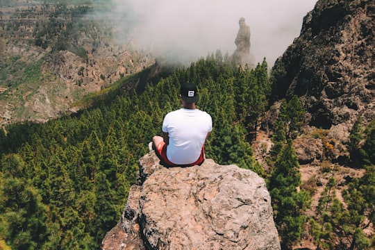 man sitting on cliff wearing white T-shirt in Roque Nublo Spain