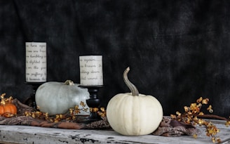 white and grey pumpkin near two white pillar candles on a fall decor