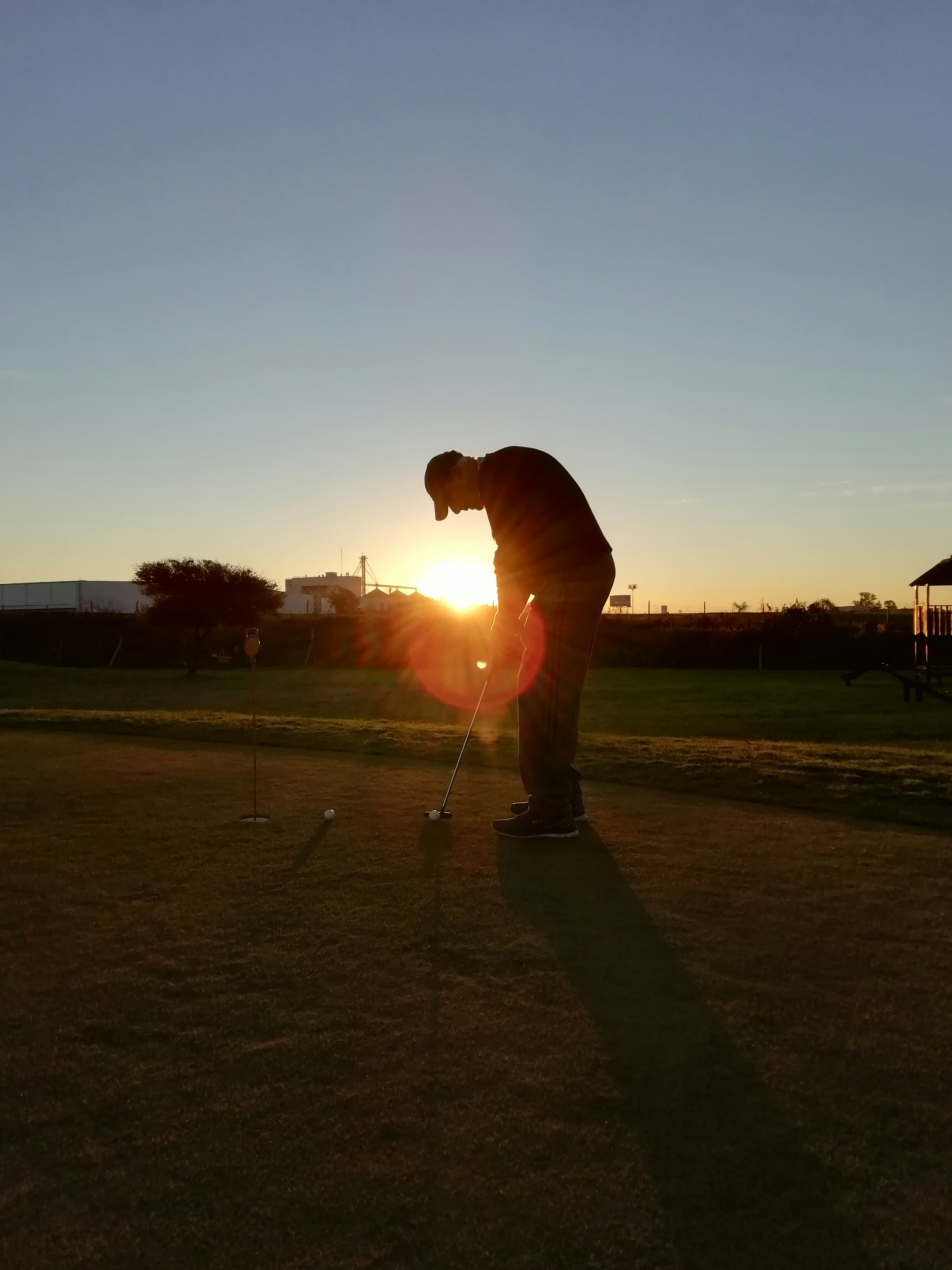 Golfer at sunset on a course, silhouette against golden sky, dramatic light