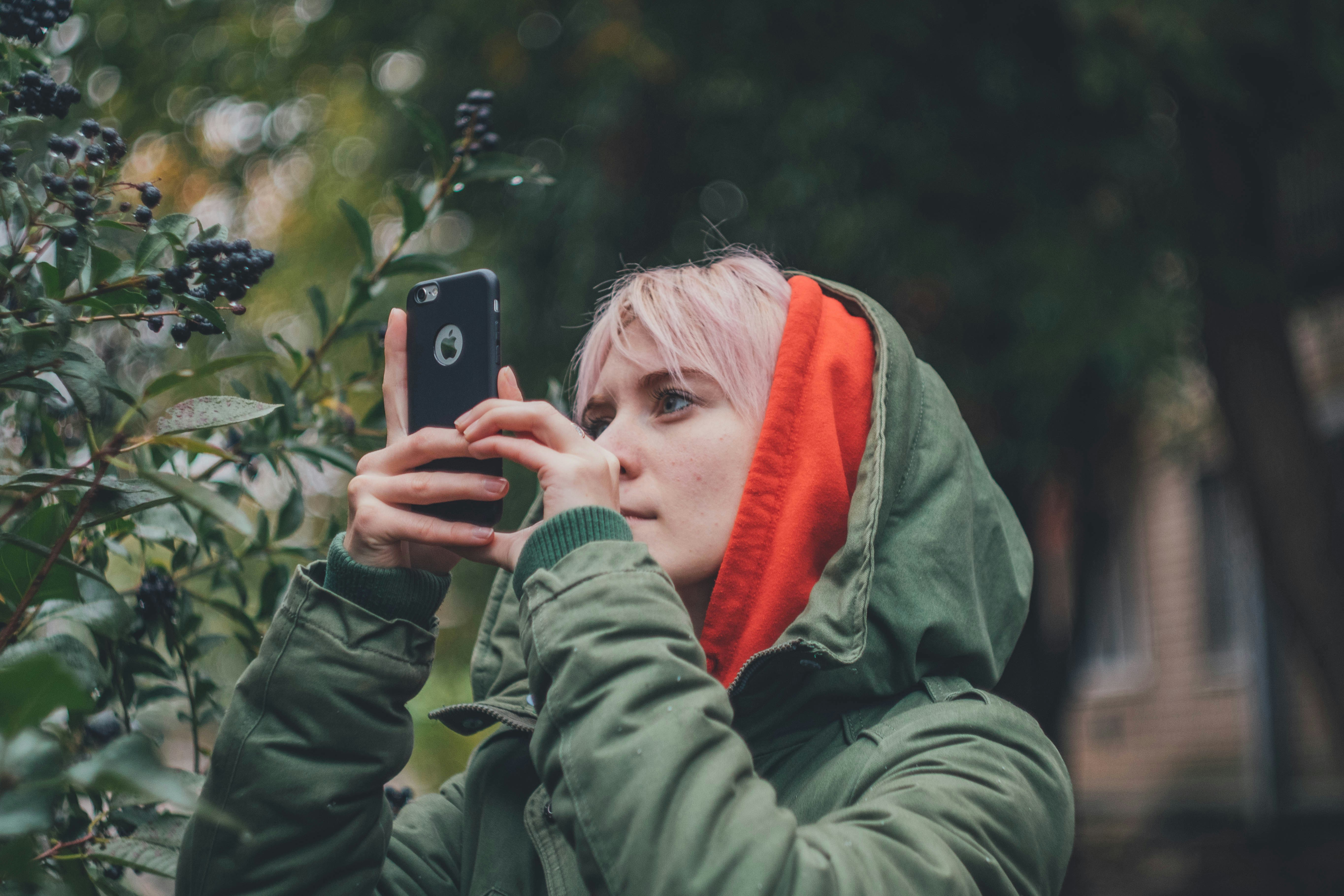 woman wearing green hooded jacket holding iPhone