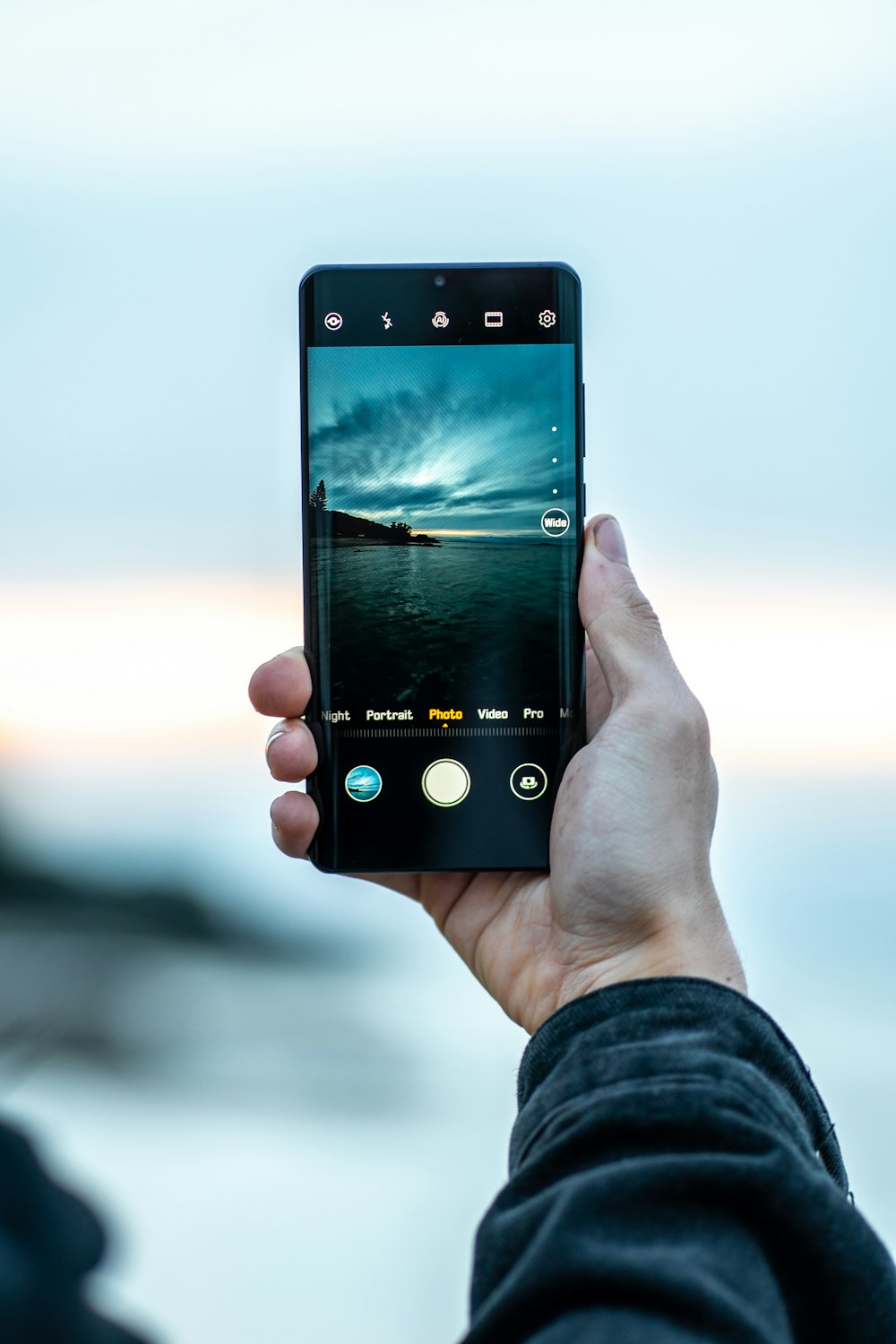 person using smartphone taking photo of body of water