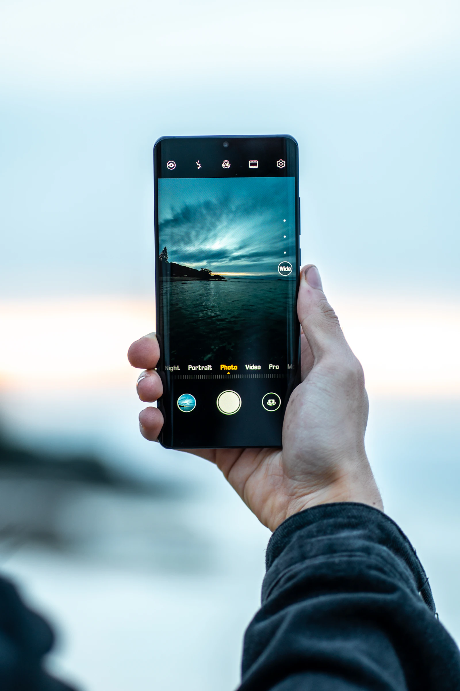 Person holding a smartphone near open water at sunset