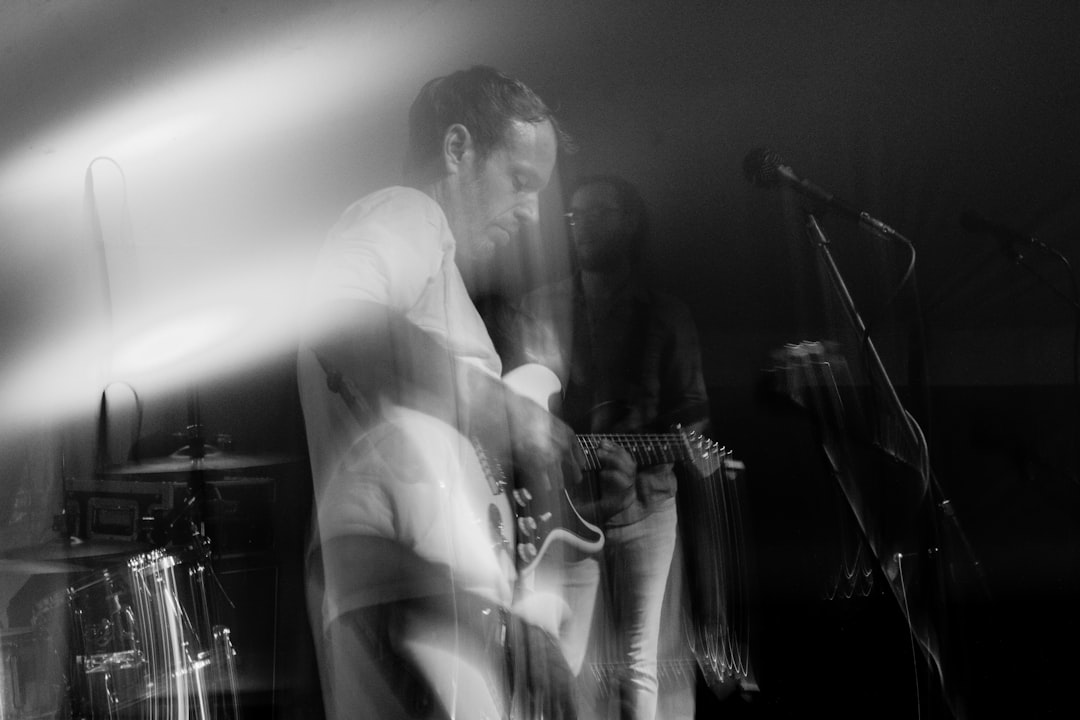 grayscale photography of man playing guitar