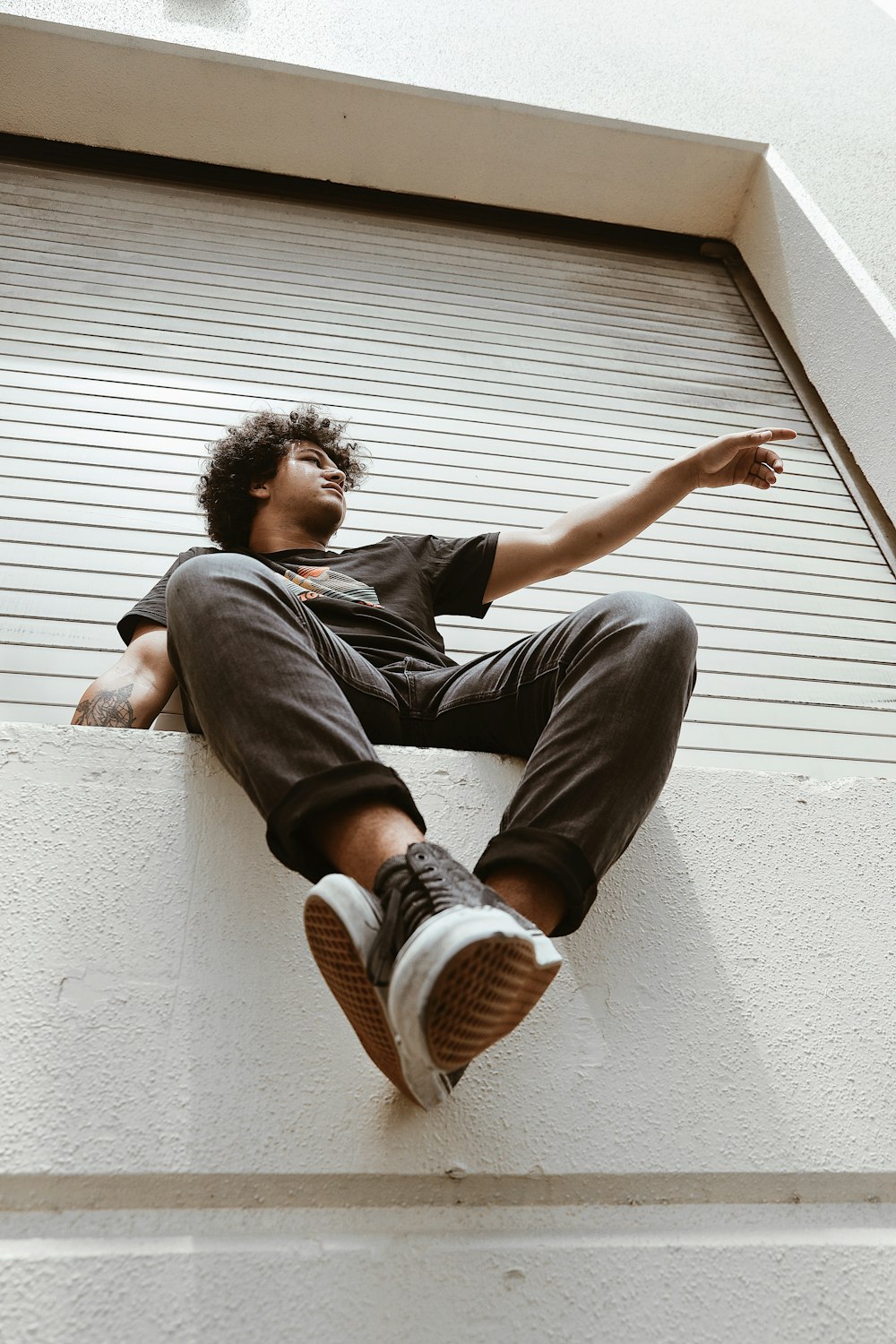 low angle photography of man sitting beside roll-up door during daytime