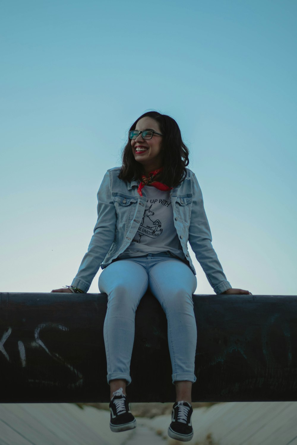 Mujer sonriente con chaqueta de mezclilla azul sentada en una superficie de concreto negro durante el día