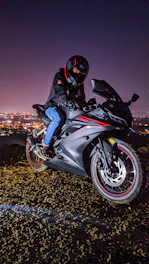 A dynamic photo of a rider wearing a red and black helmet and jacket, cruising on a sleek motorcycle at sunset.
