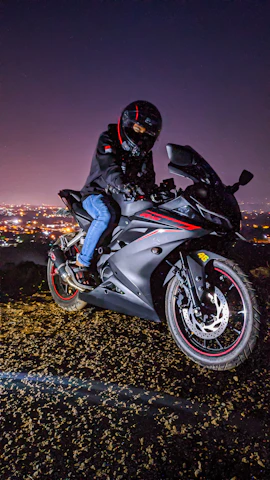 A dynamic photo of a rider wearing a red and black helmet and jacket, cruising on a sleek motorcycle at sunset.