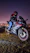 A smiling rider wearing a helmet, sitting on a sleek motorcycle against a bustling city street backdrop.