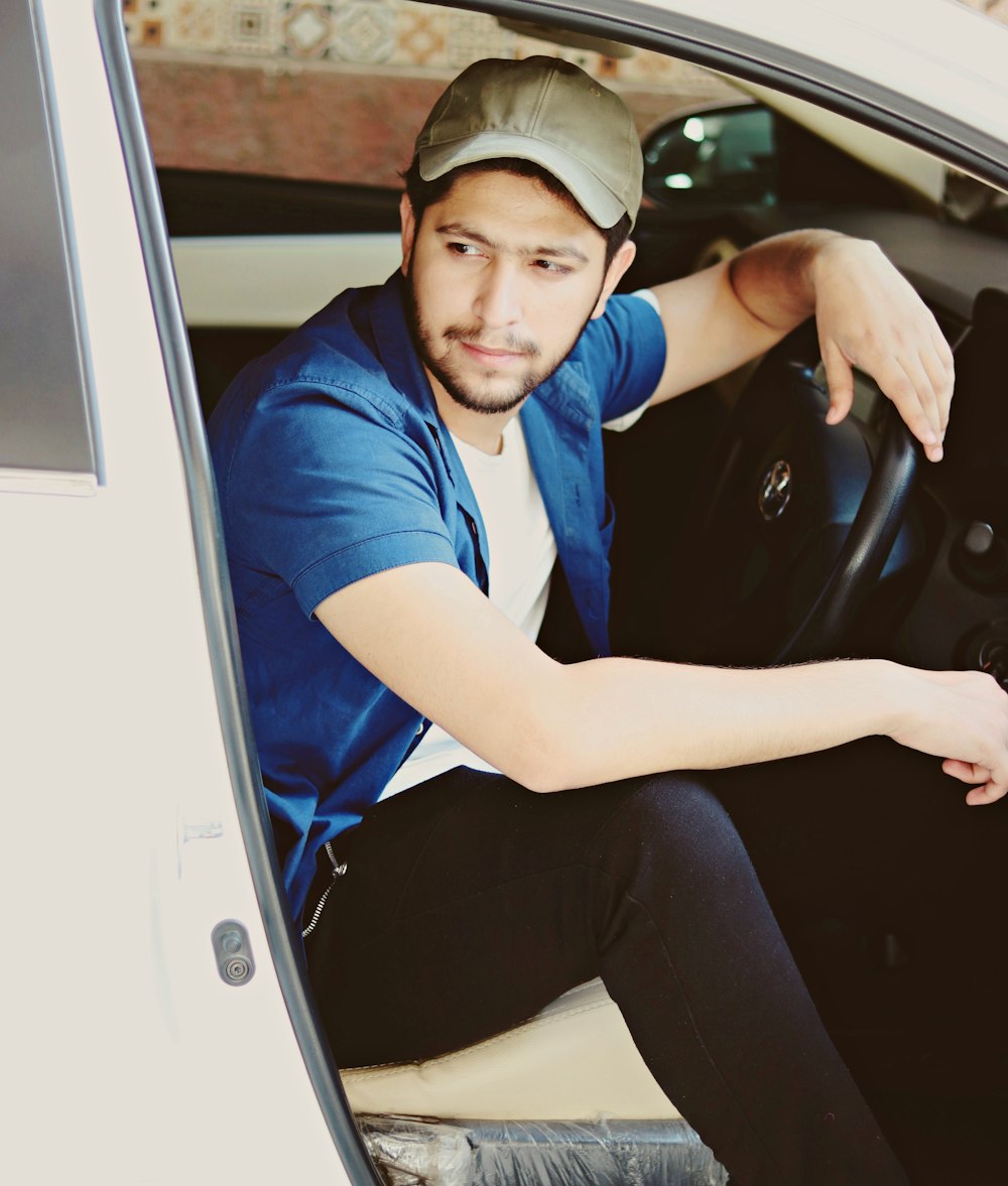 man sitting on driver's seat of a car with opened door looking at his right