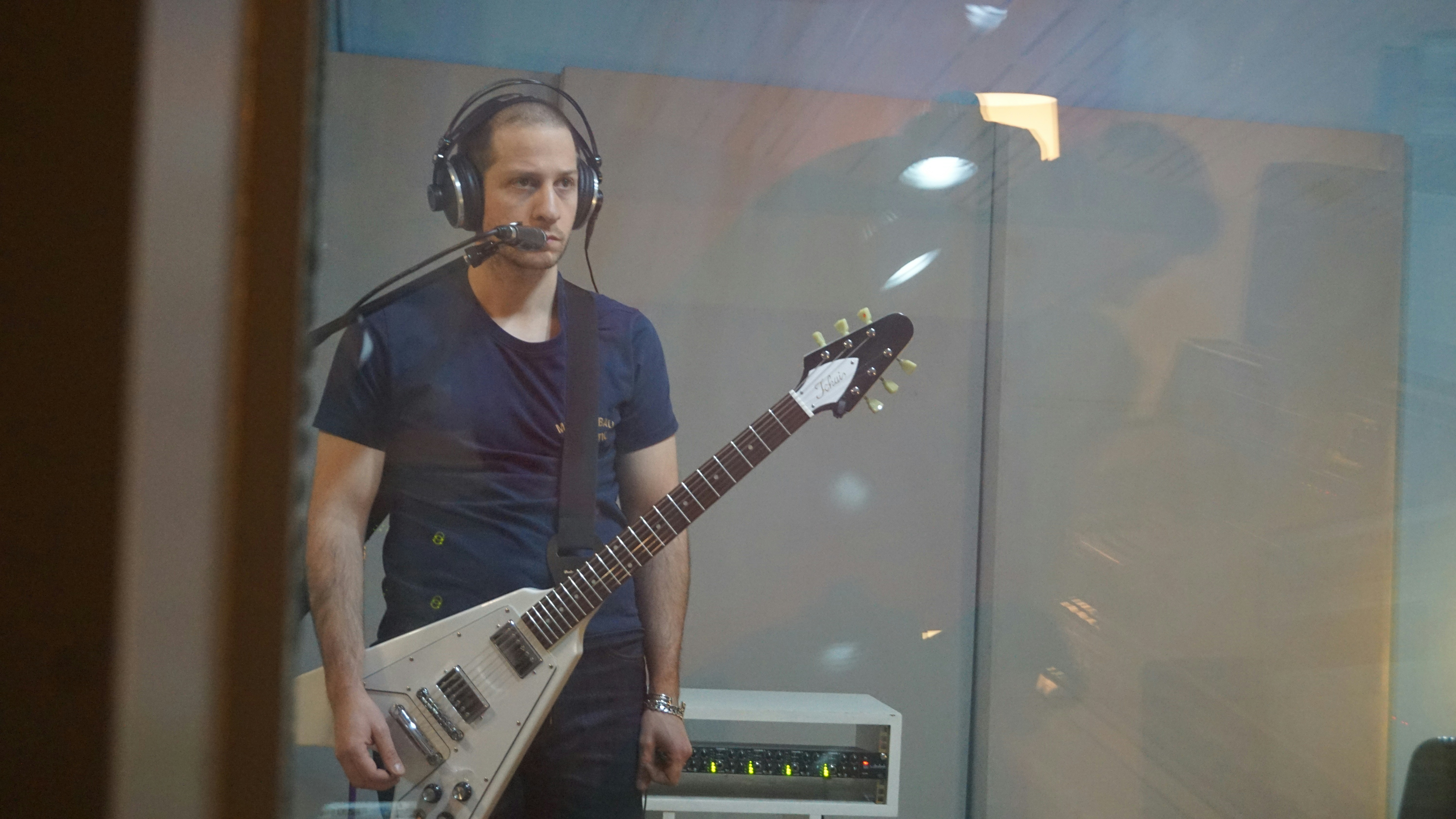 Zrozpaczony gitarzysta po podłączeniu cyfrowego modelera do przypadkowego wzmacniacza na próbie, porównujący to do idealnego brzmienia w słuchawkach, z wyrazem frustracji na twarzy.