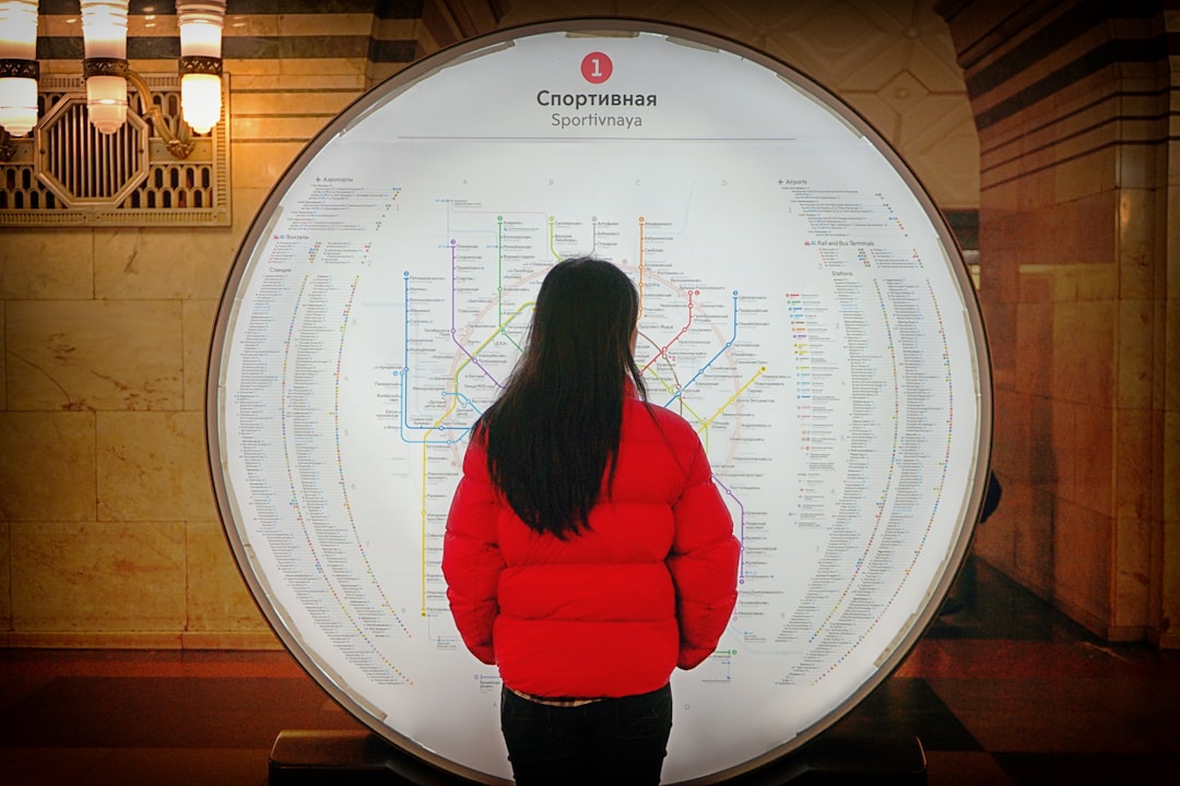 woman in red bubble jacket standing in front of round sign