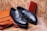 A pair of black leather loafers with tassel detailing is placed on a brown leather briefcase. A red leather wallet is set against a marble-textured background, creating a luxurious and elegant arrangement.