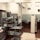 A professional kitchen setting with stainless steel shelves and countertops, featuring an array of kitchen supplies and equipment. The room has tiled flooring and walls, with various silver and gray tones dominating the decor.