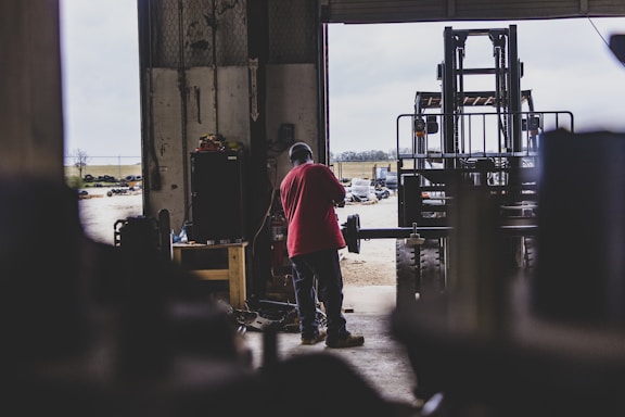 A friendly customer service representative wearing a red shirt with heavy equipment in the background.