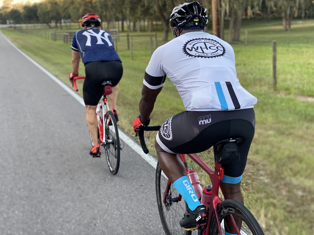two men riding road bikes at the side of the road during day