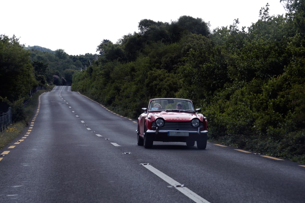 red coupe on road near trees during daytime