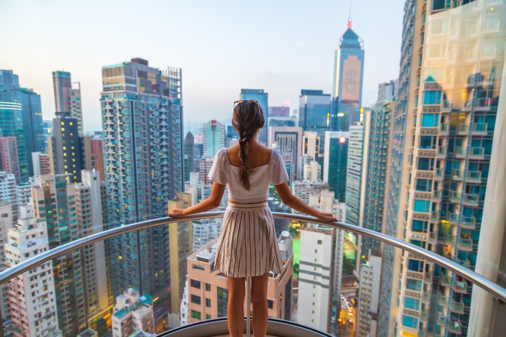 woman standing near gray stainless steel railings viewing city with high-rise buildings during daytime