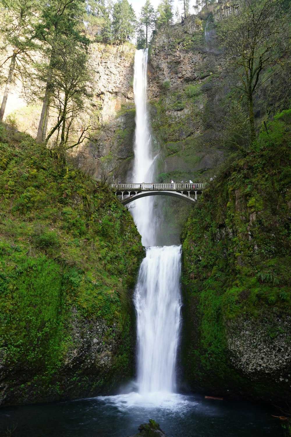 concrete bridge across on waterfalls at daytime