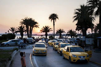 A taxi cruising along a scenic coastal road near a ferry terminal at sunset.