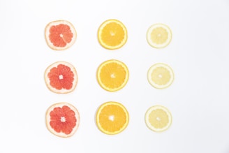 Slices of citrus fruits are neatly arranged in a grid pattern on a white background. The fruits include grapefruit, orange, and lemon. The slices are evenly spaced and showcase the vibrant colors and textures of the fruit.