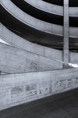 A spiral ramp structure made of concrete, showing an architectural design with repetitive patterns and smooth curves. The surface of the concrete displays a raw texture with visible marks and joins.