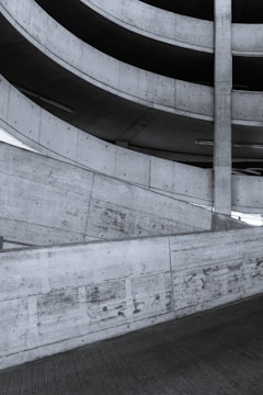 A spiral ramp structure made of concrete, showing an architectural design with repetitive patterns and smooth curves. The surface of the concrete displays a raw texture with visible marks and joins.