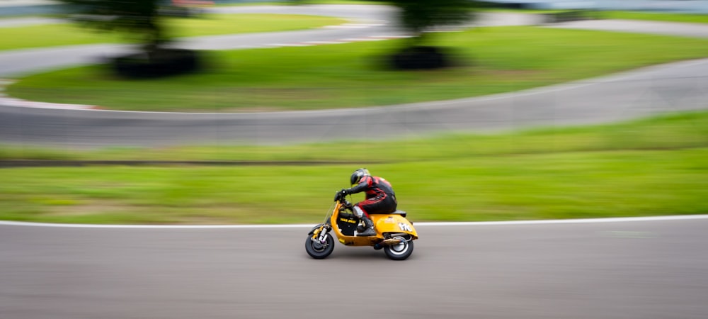 man riding yellow motor scooter on road