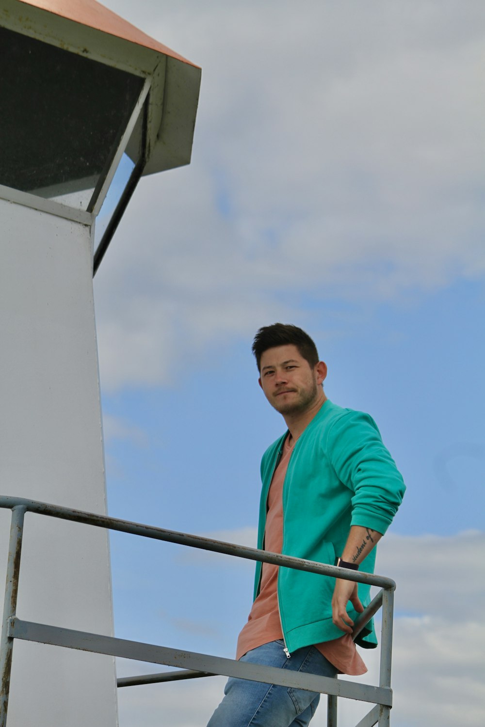 a man in a green jacket standing on a metal railing