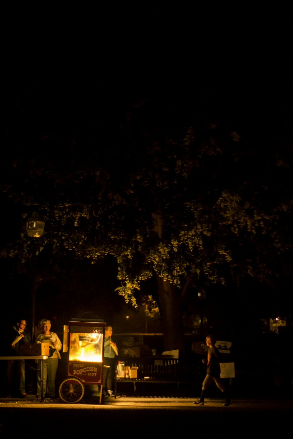 a group of people standing around a food cart at night