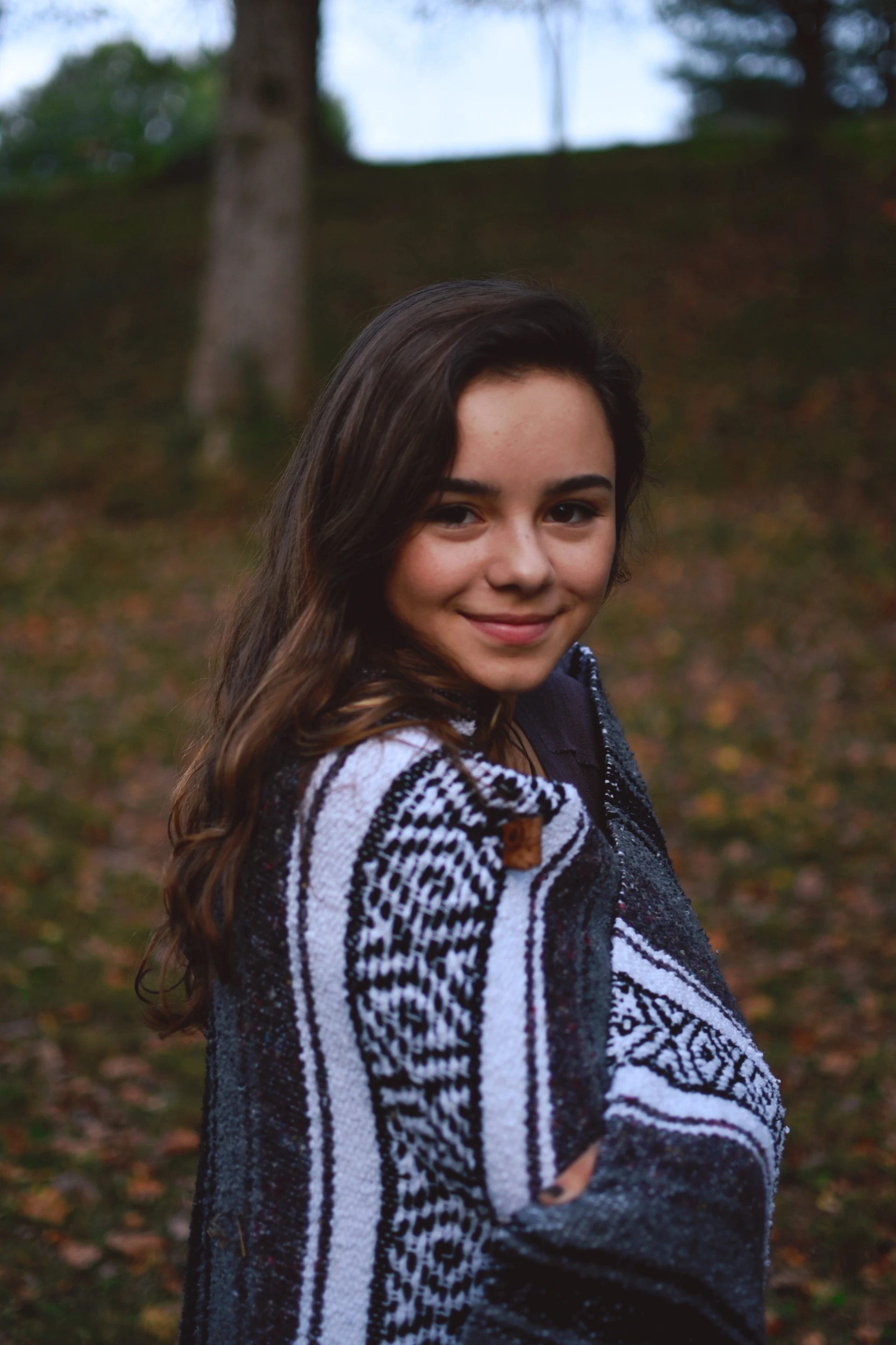 A cozy model wearing a vibrant Altessa poncho standing against the backdrop of the Ecuadorian Andes at sunset.