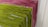 Racks of pasta are hanging side by side, with varying colors indicating different types or flavors. The pasta is neatly arranged and appears to be freshly made, showcasing green and pink hues.