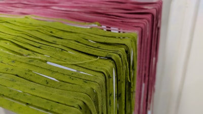 Racks of pasta are hanging side by side, with varying colors indicating different types or flavors. The pasta is neatly arranged and appears to be freshly made, showcasing green and pink hues.