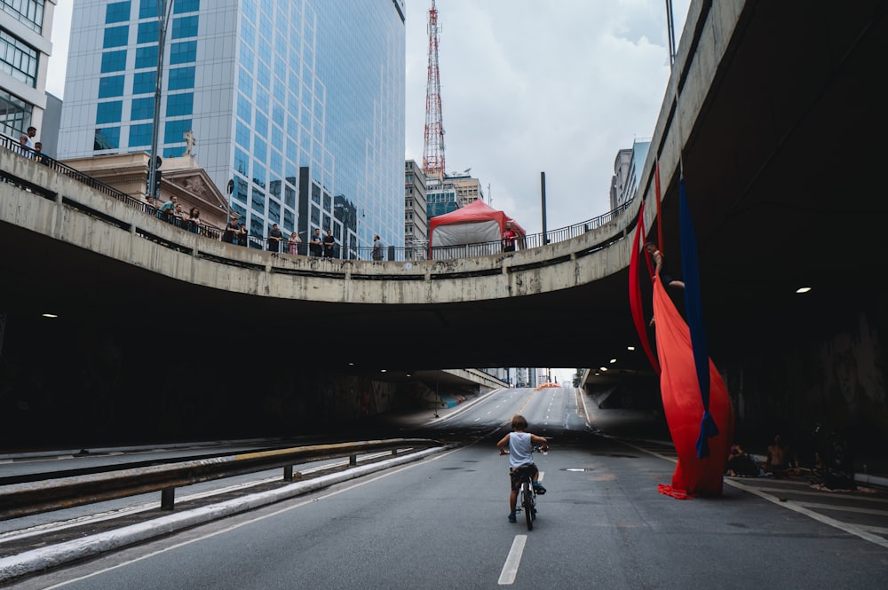 a man riding a bike down a street under a bridge