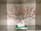 A decorative sculpture features a white deer sitting on a green pedestal. Above the deer, there are artistic branches with red flowers, creating a visually striking arrangement. The sculpture is showcased in a display box with soft lighting.