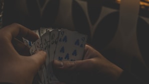 Hands holding playing cards over a poker table in a dimly lit room.
