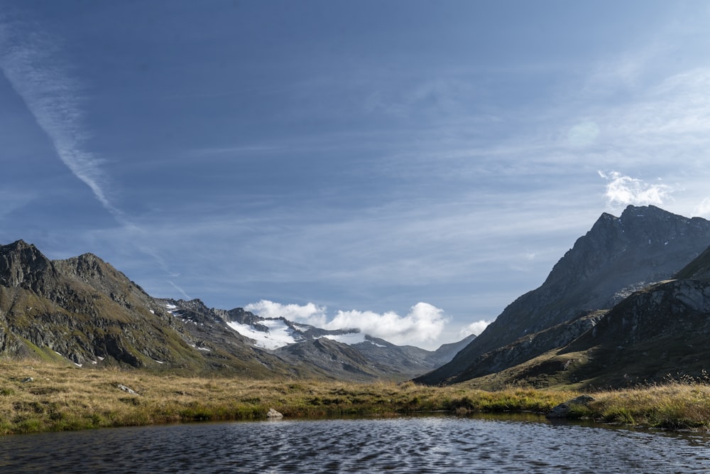 body of water, grass field, and mountains during day