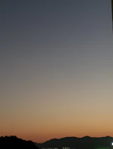 A serene twilight landscape with soft purple and orange hues behind mountain silhouettes.