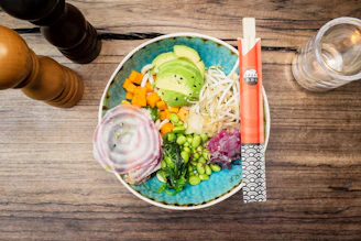 A colorful bowl of fresh vegetables, grains, and lean protein arranged artfully on a dark table.