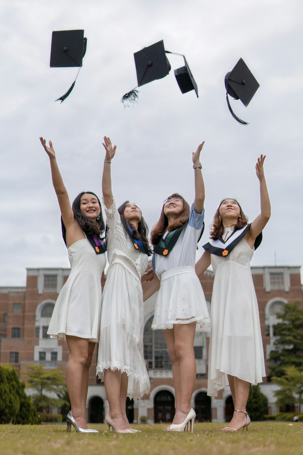 Fotografía de ángulo bajo de cuatro chicas lanzando sombrero de mortero cerca del exterior durante el día