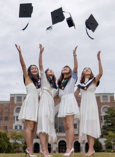 low-angle photography of four girls throwing mortar hat near outdoor during daytime