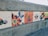 A series of hand-painted tiles mounted on a concrete wall featuring various abstract designs, including butterflies, abstract shapes, and bold colors. One tile reads 'The Attics' with some artistic brush strokes.