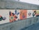 A series of hand-painted tiles mounted on a concrete wall featuring various abstract designs, including butterflies, abstract shapes, and bold colors. One tile reads 'The Attics' with some artistic brush strokes.