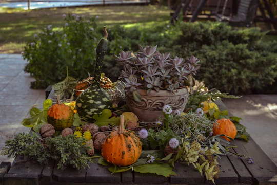 A child's hands arranging colorful autumn leaves and pinecones on a wooden table outdoors.