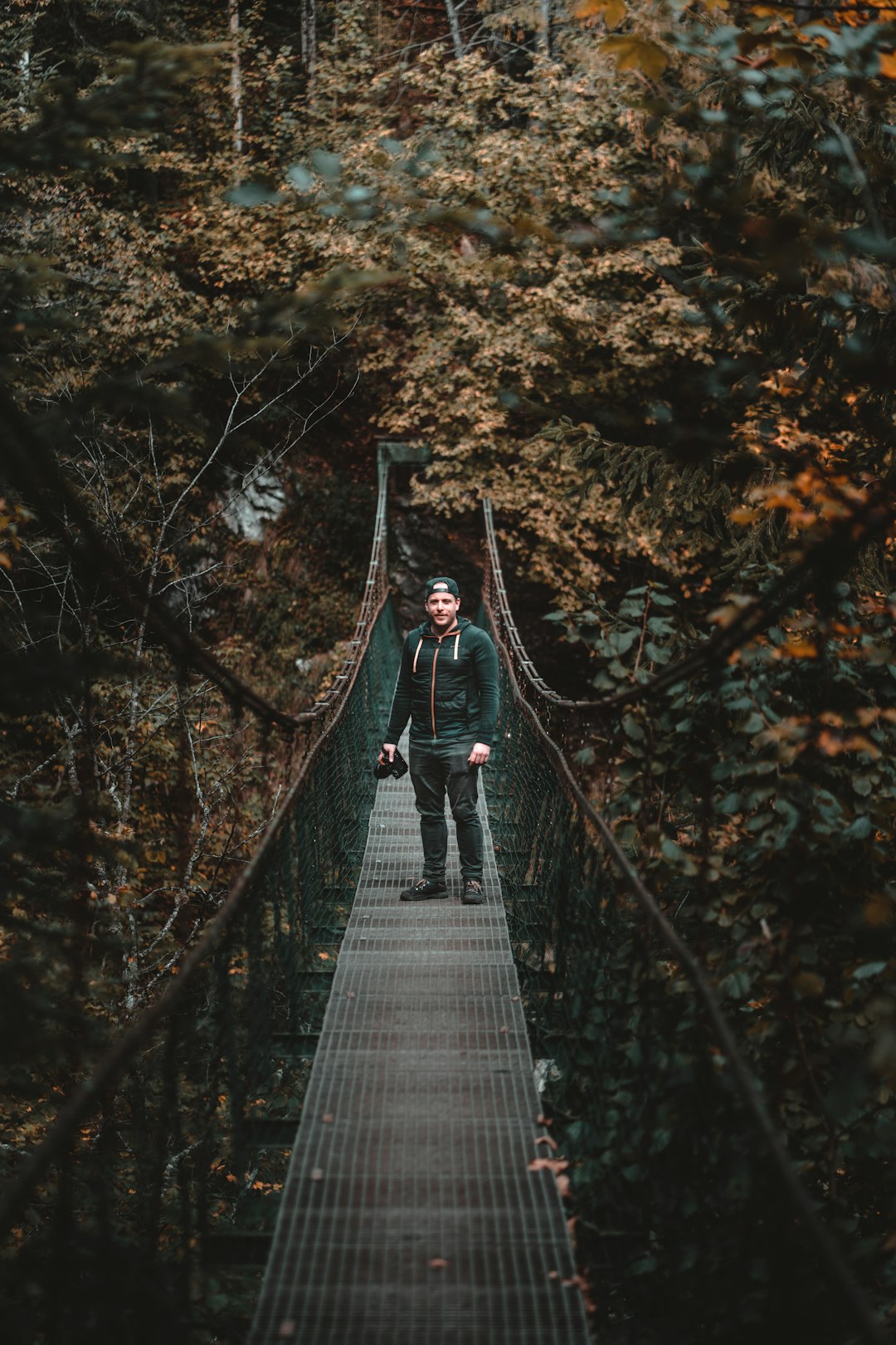 man wearing jacket and pants standing on bridge near trees