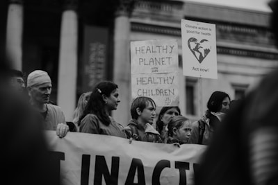 A group of people participating in a protest, holding signs with messages about climate action and health. The signs contain slogans like 'Healthy Planet Healthy Children' and 'Climate action is good for health. Act now!' The atmosphere appears serious and determined.
