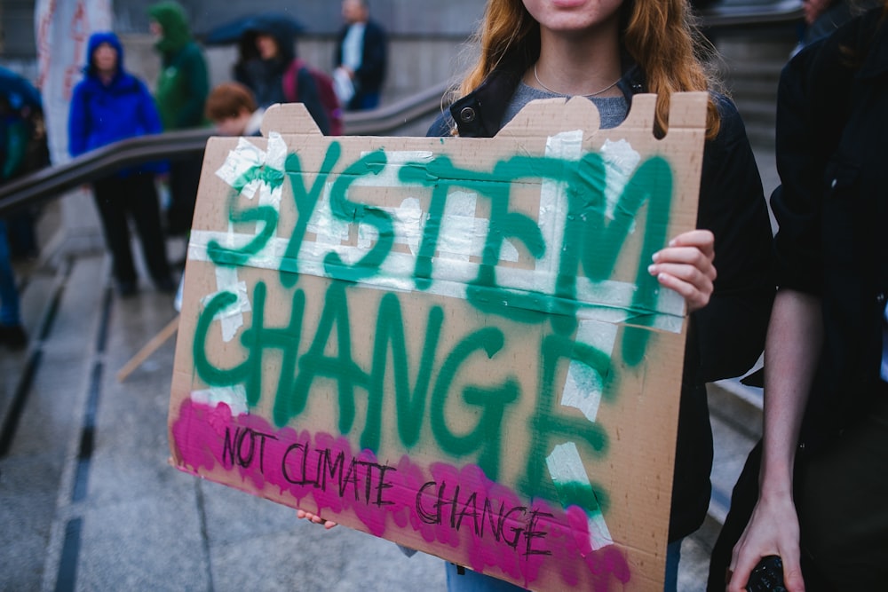 woman holding system change not climate change sign