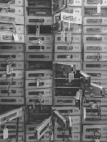 An array of numbered metal safety deposit boxes, many of which are open, each with a key and tag hanging from the lock.